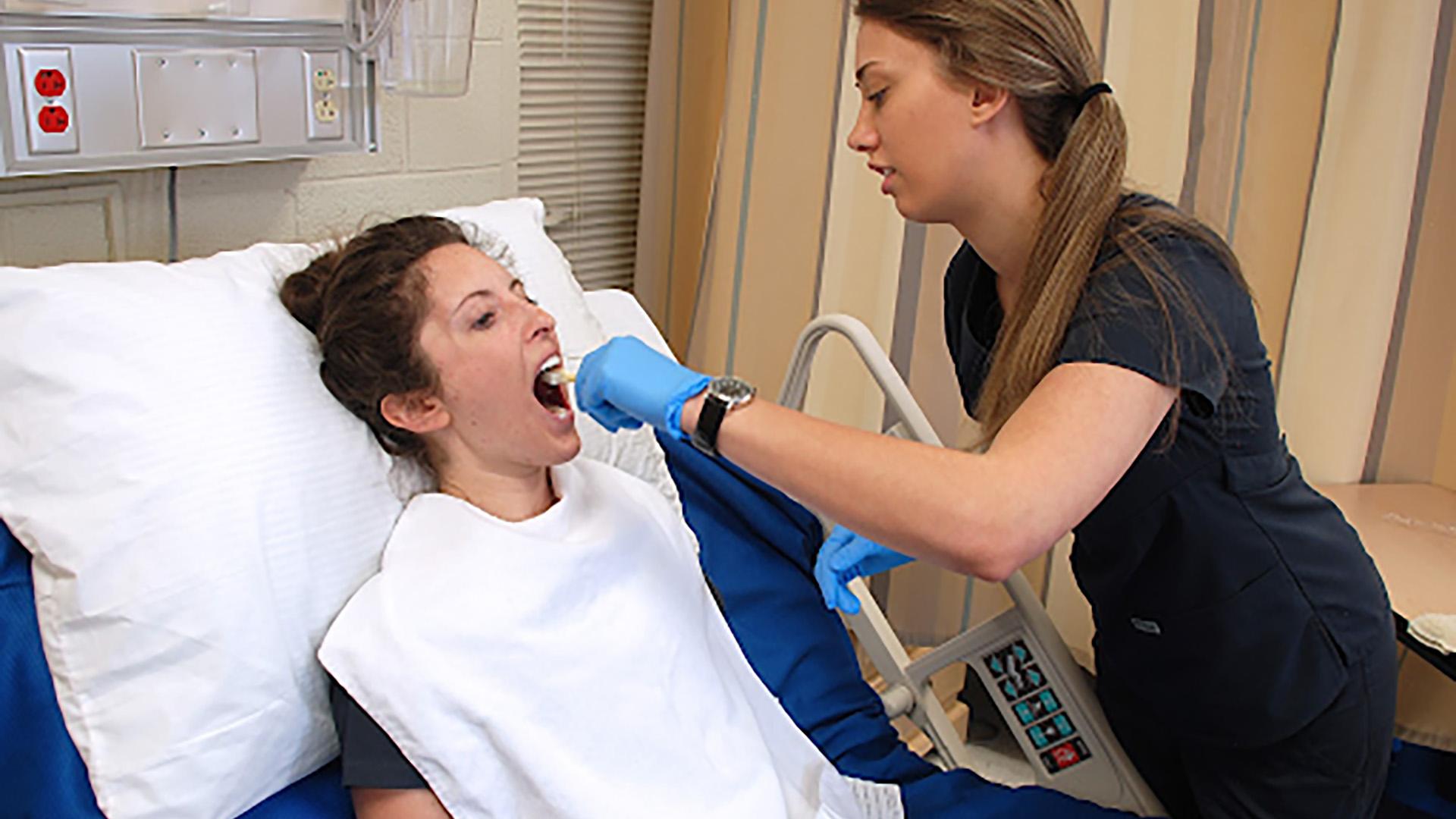 2 individuals in a medical setting, one on a hospital bed and one conducting a health-check up